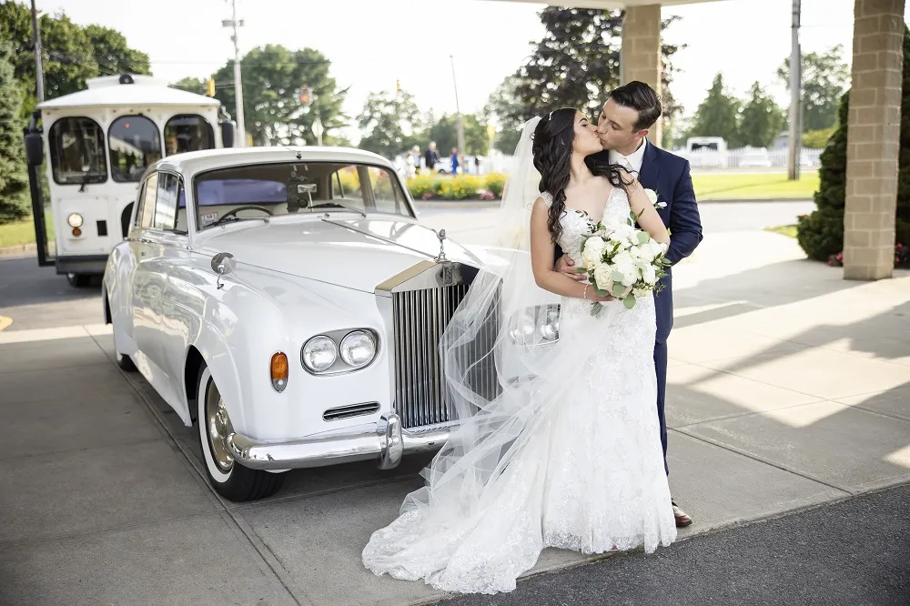 Bride and groom sharing a kiss in front of a white rolls royce after an aisle reveal wedding at Kirkbrae country Club