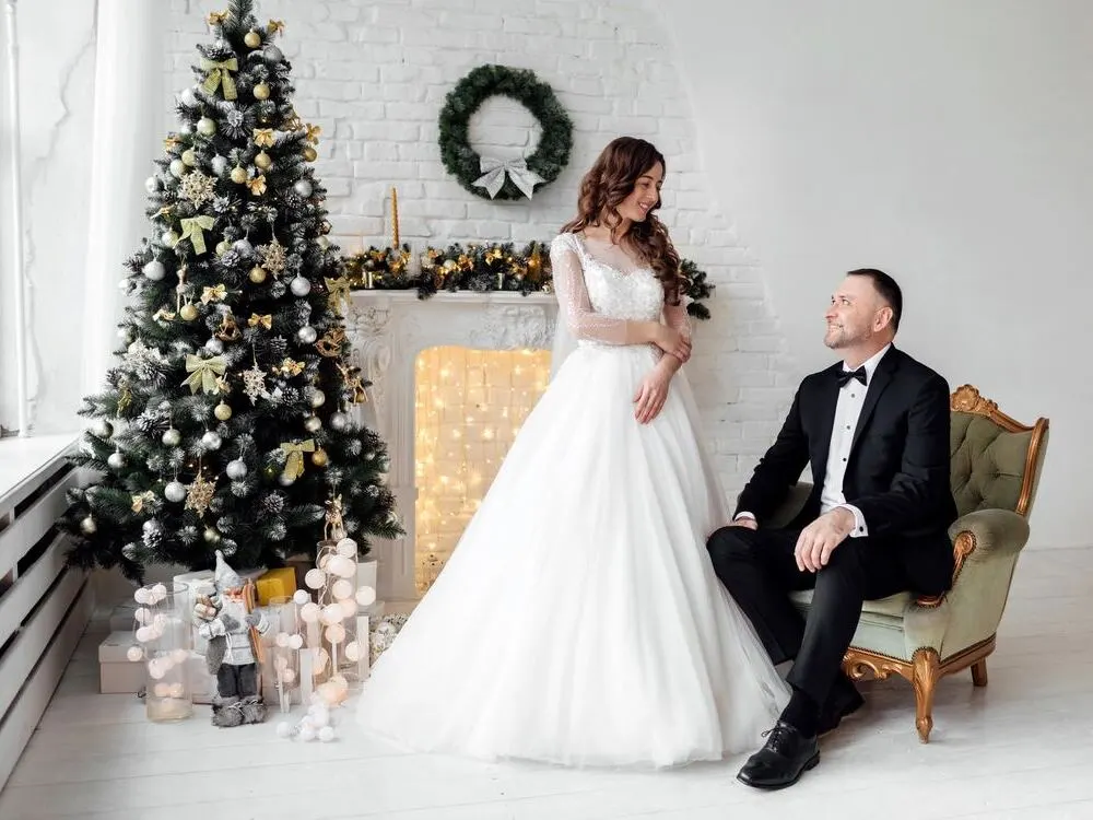Bride and groom posing in an elegant Christmas themed wedding setting with a decorated tree and fireplace.