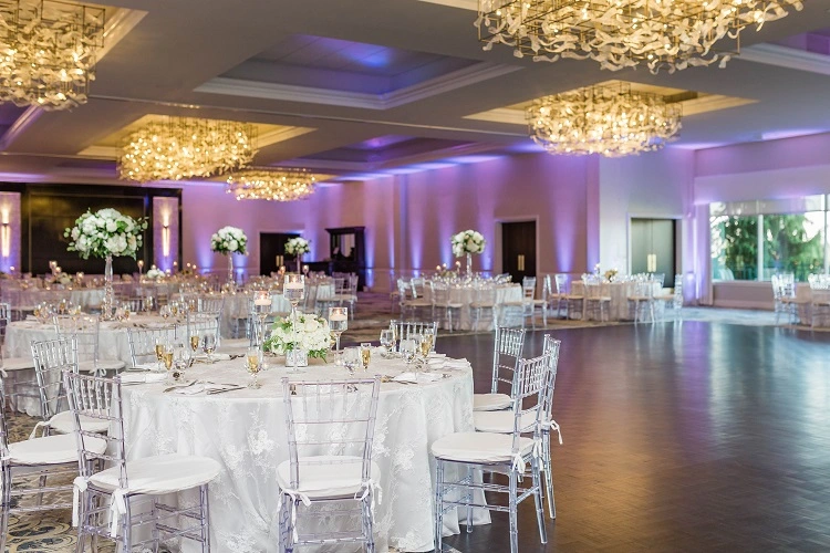 Wedding tables setup in grand ballroom under chandelier with silver chairs
