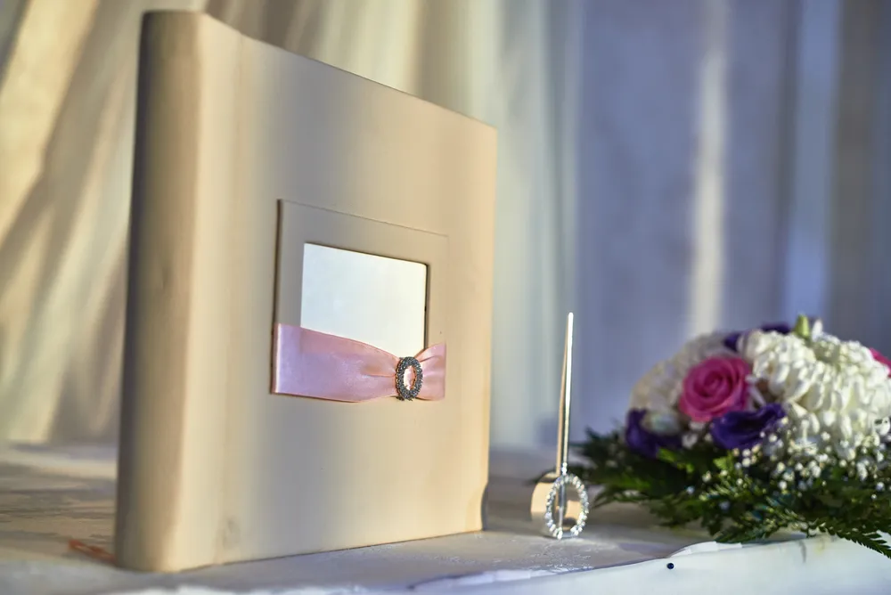 Wedding guest book standing on a wedding table with a pen and floral arrangement next to it