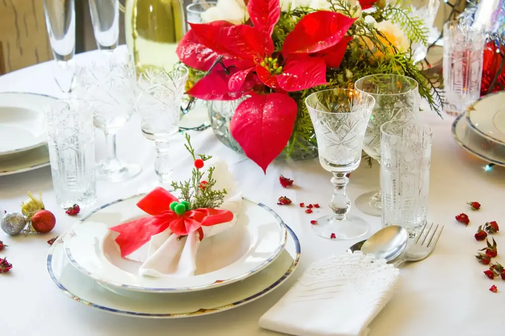 Festive holiday table arrangement featuring a red poinsettia centerpiece, crystal glasses, and a Christmas-themed place setting.