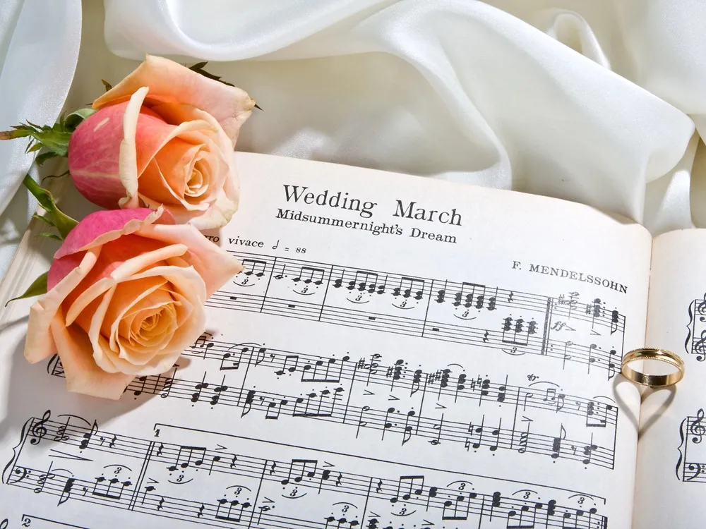 Music note shee with ornately decorated floral arrangement sitting on top of it with a wedding band