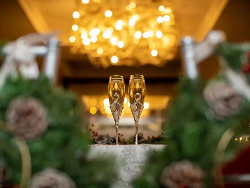 Two champagne glasses ready to toast by bride and groom underneath a chandelier